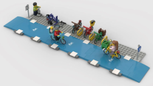 A bike lane made of lego, with bike parking and two lego people travelling by bike, one with a baby on the back and the other with a crate full of groceries on the front.